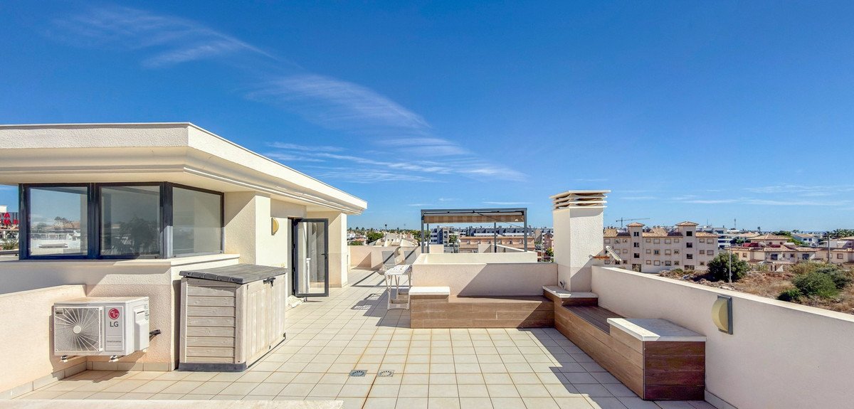 Rooftop terrace with tiled flooring, seating, and city view under blue sky
