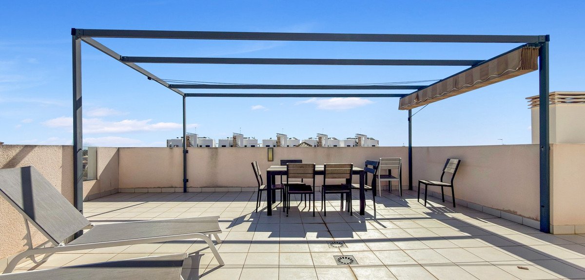 Rooftop terrace with pergola, dining table, chairs, and lounge chair under clear blue sky