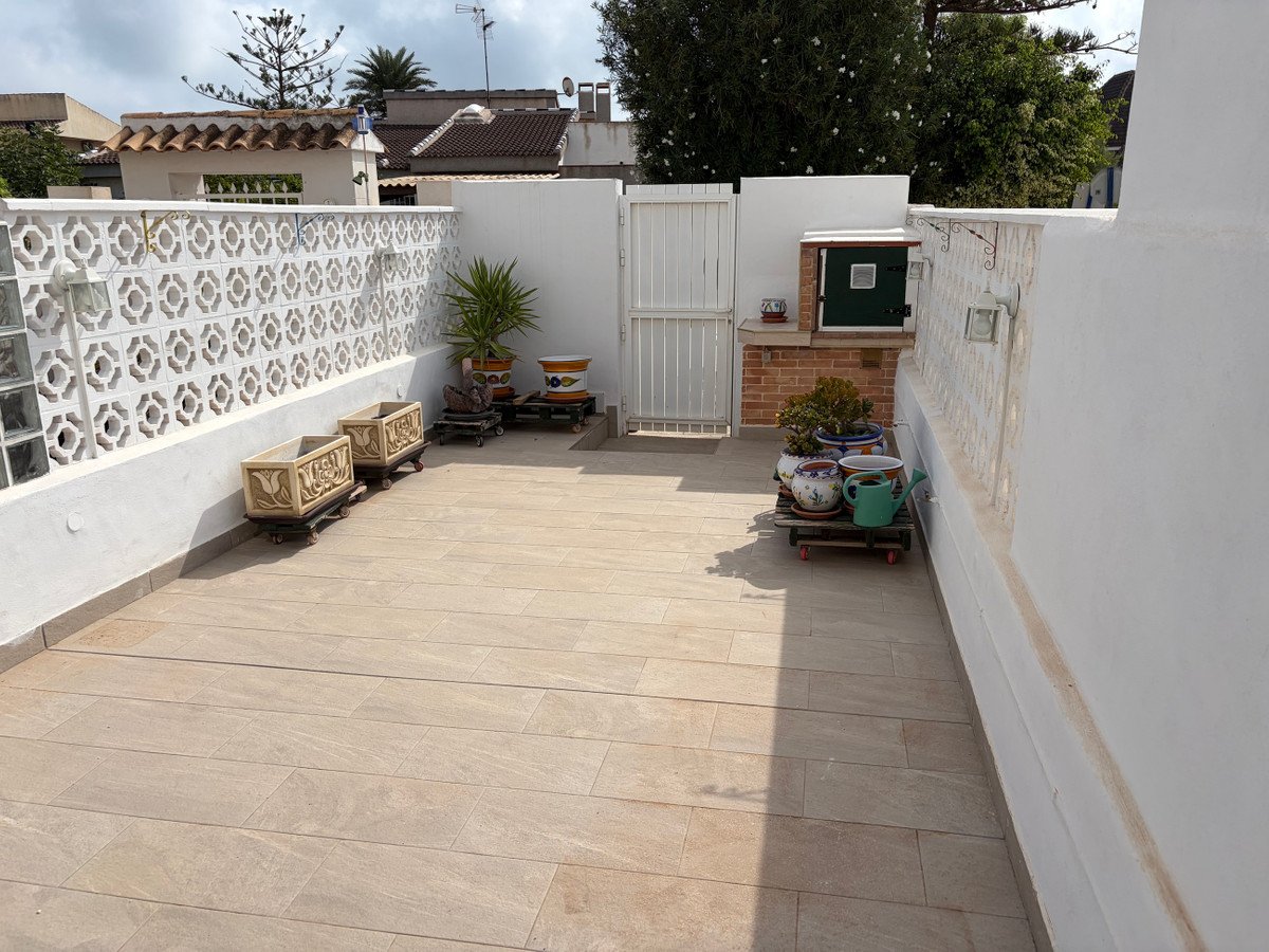 A tiled patio with decorative planters, a white fence, and an outdoor brick grill area.