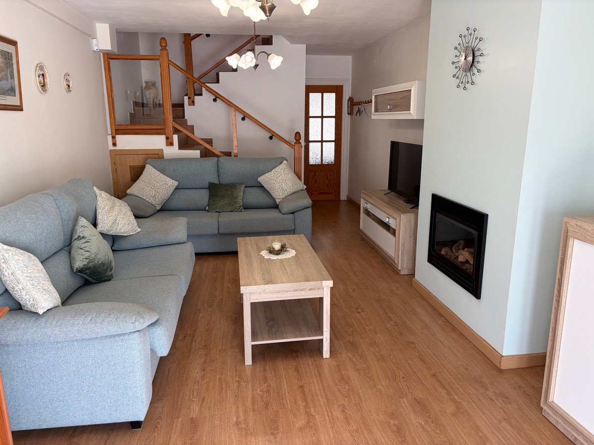 A cozy living room with blue sofas, a fireplace, television, and a staircase leading upstairs.