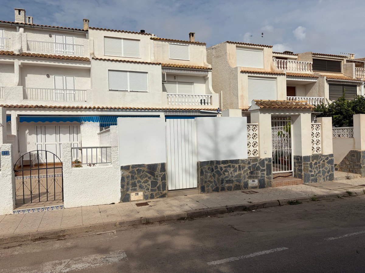 Exterior view of a white townhouse with balconies, shutters, and a gated entrance on a street.