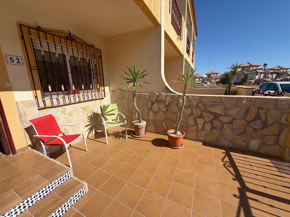 Terrace with tiled flooring, two chairs, potted plants, and a stone wall overlooking a residential street.