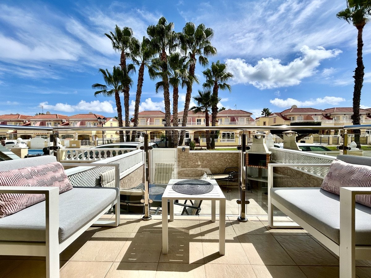 A sunny terrace with palm trees, seating area, and a view of residential buildings.