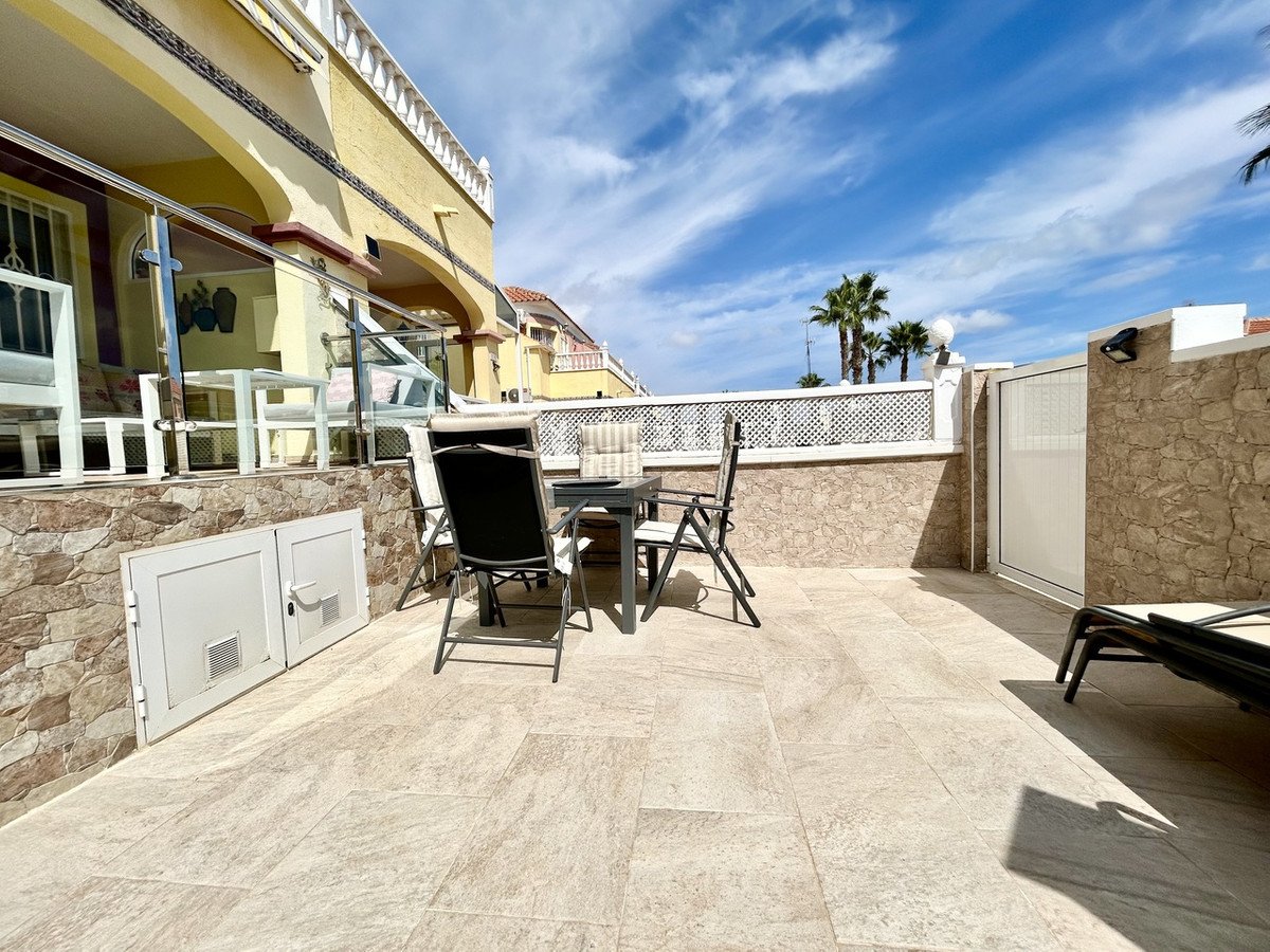 A spacious tiled terrace with outdoor seating, a table, and a sun lounger, offering a view of palm trees under a blue sky.