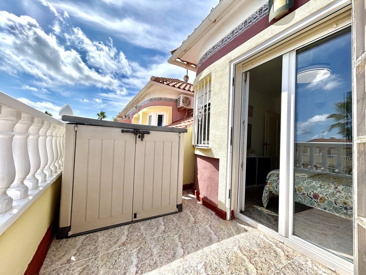 Balcony view with a storage unit, looking into a bedroom with a patterned bedspread. Sunny day with clouds.