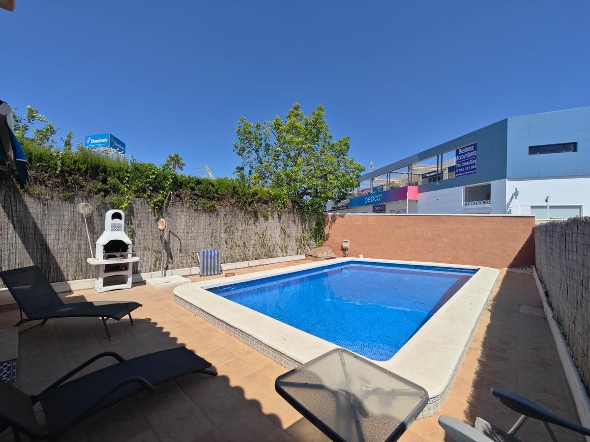 Private pool area with lounge chairs, BBQ, and greenery under a clear blue sky.