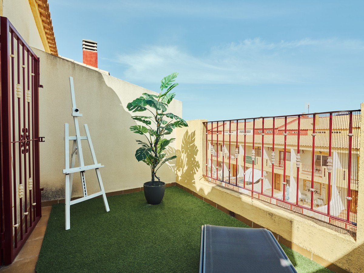A terrace with artificial grass, a plant, an easel, and a lounge chair with a view of buildings.