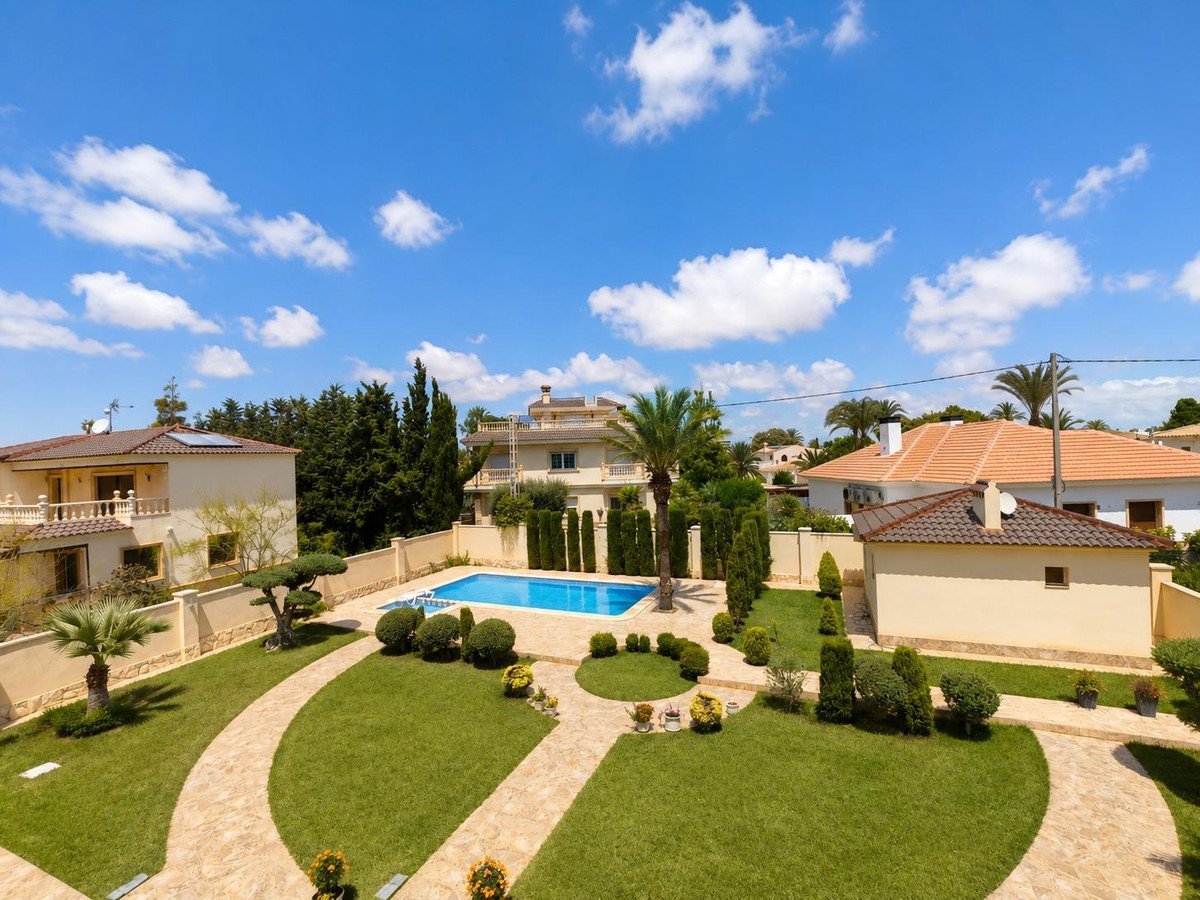 Beautiful villa with a swimming pool, manicured garden, and palm trees under a blue sky.