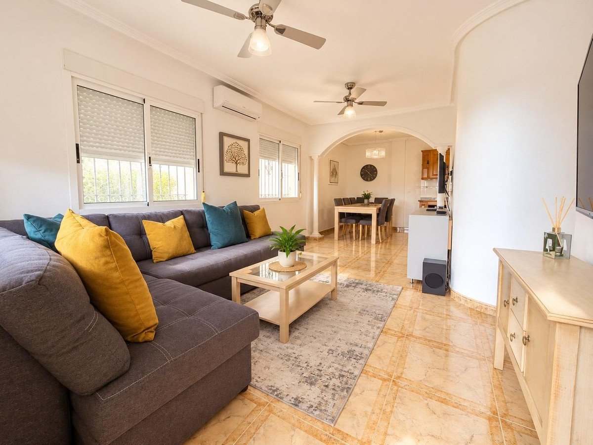 Spacious living and dining room with an L-shaped grey sofa, colorful cushions, coffee table, and view of the dining area.