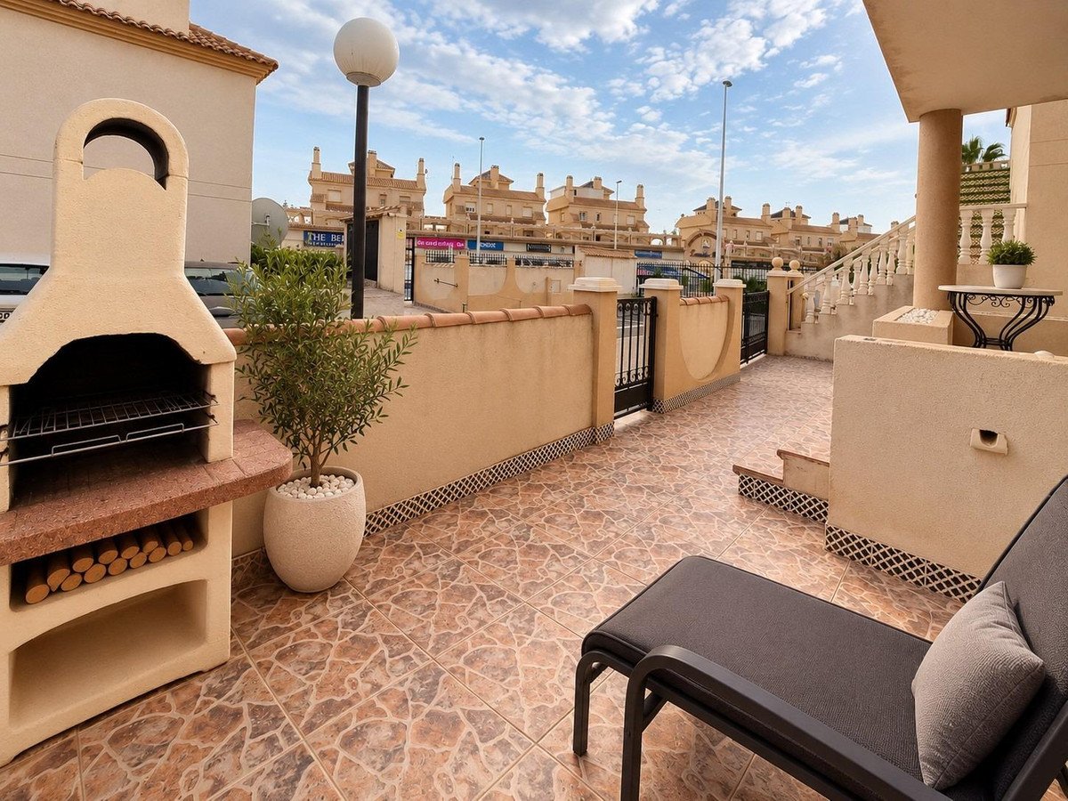 Outdoor terrace with a built-in BBQ, lounge chair, and view of residential buildings under a cloudy sky.