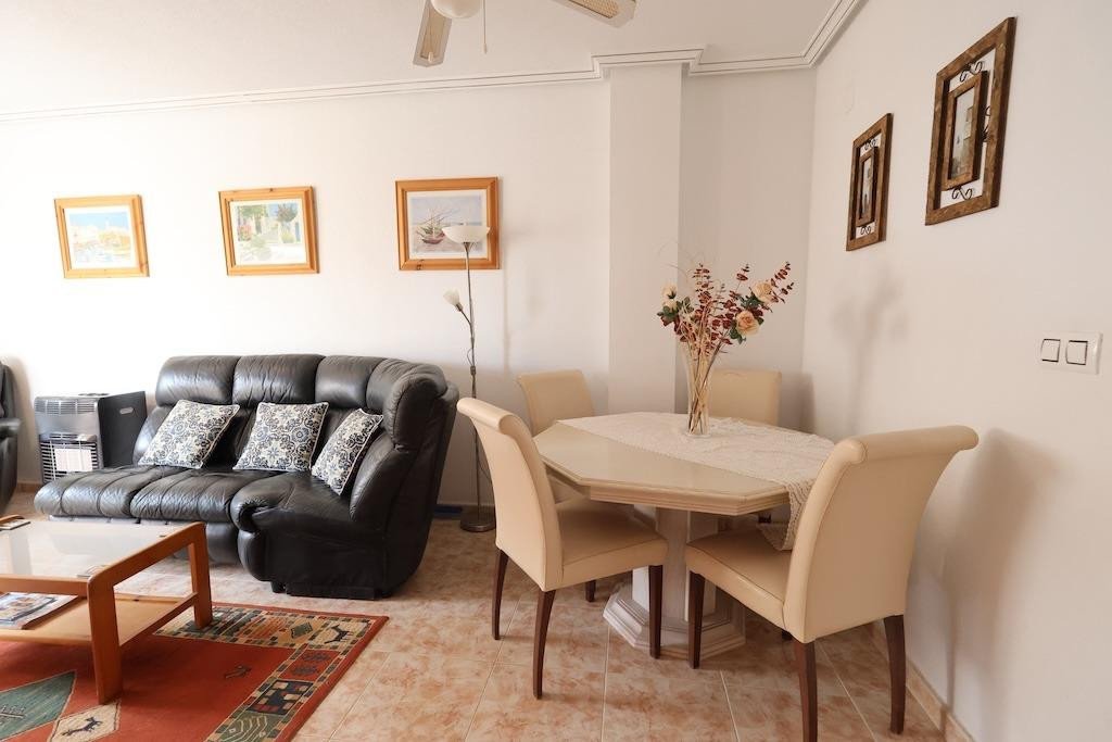 A leather sofa and dining table with chairs in a living and dining area, decorated with artwork and a vase of flowers.