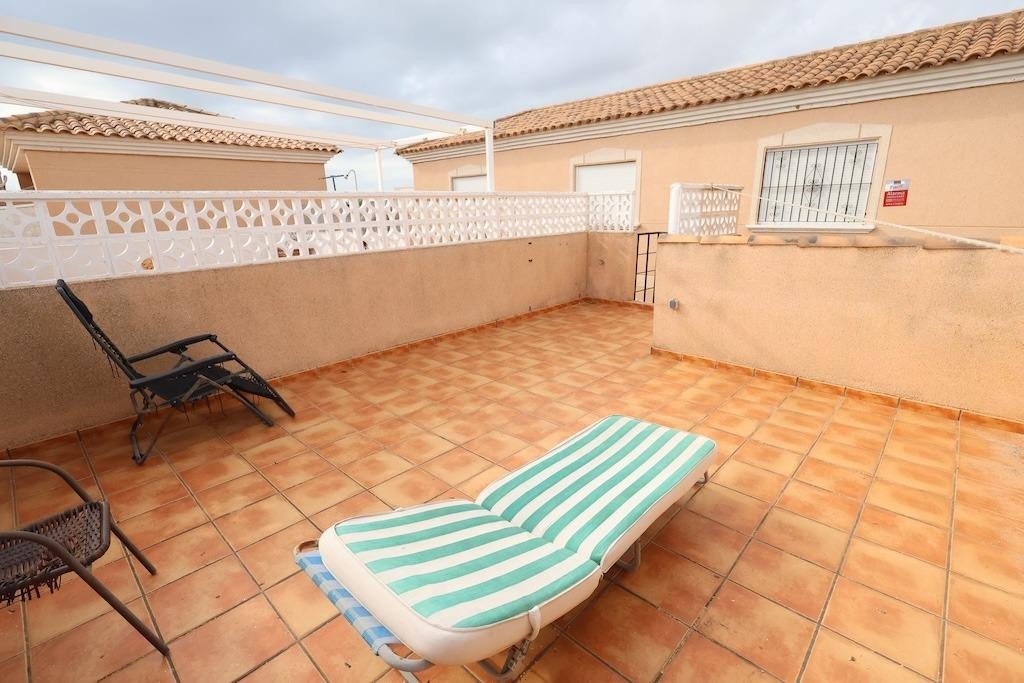 A tiled terrace with two chairs and a sun lounger, featuring a white pergola overhead.