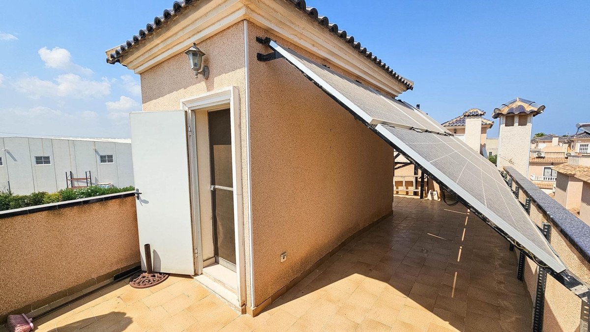 Rooftop terrace with solar panel, tiled floor, and building exterior under clear sky