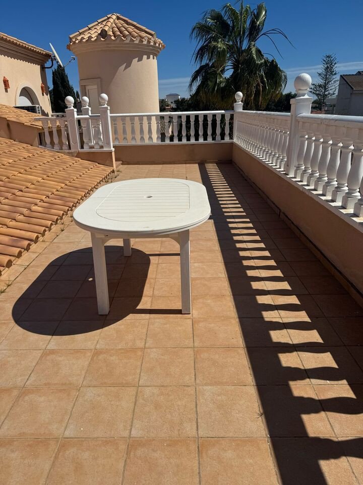 Terrace with round table, white railing, and palm trees in the background