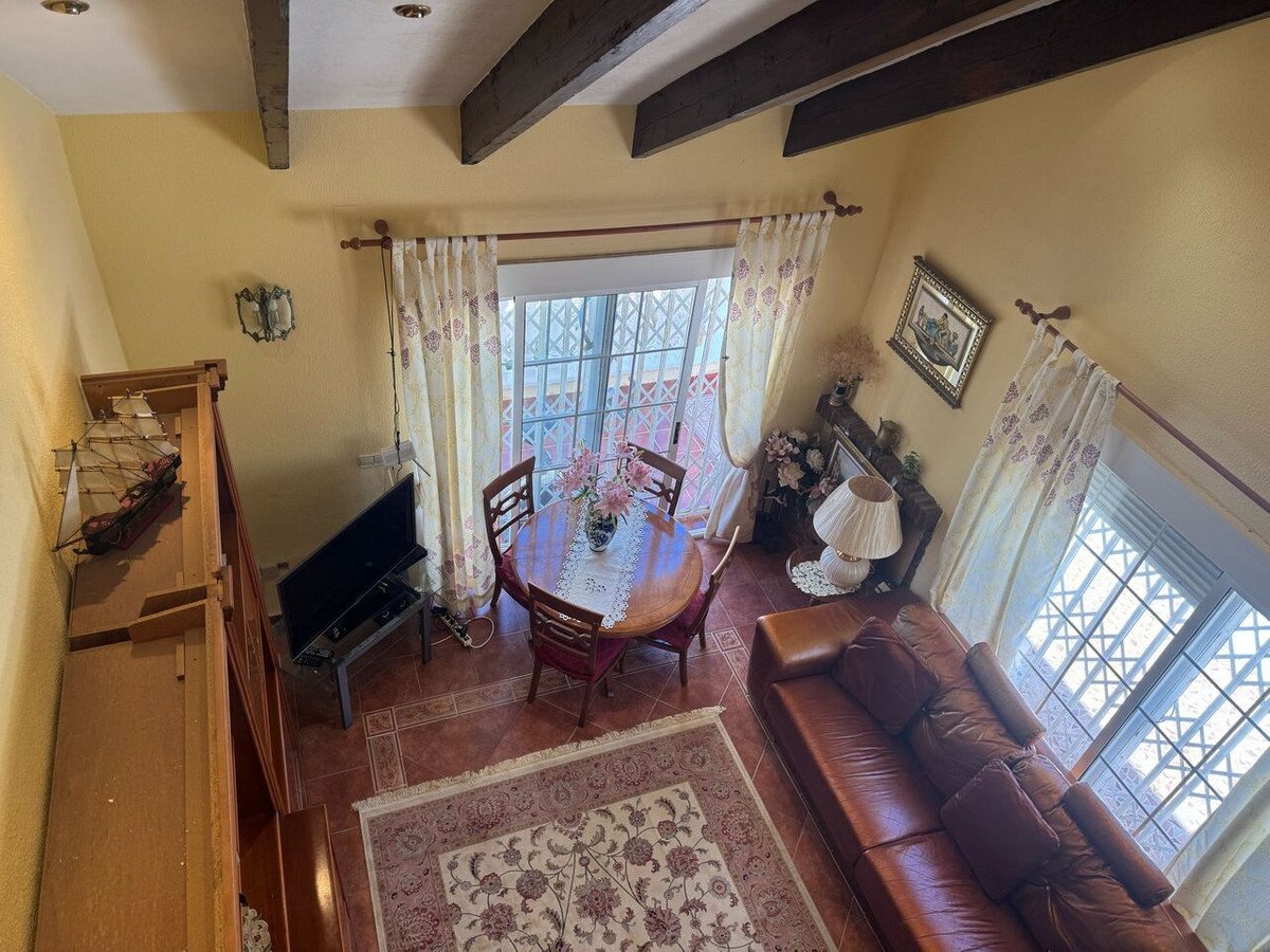 High-angle view of a cozy living room with wooden beams, leather sofa, dining table, and large windows with patterned curtains.