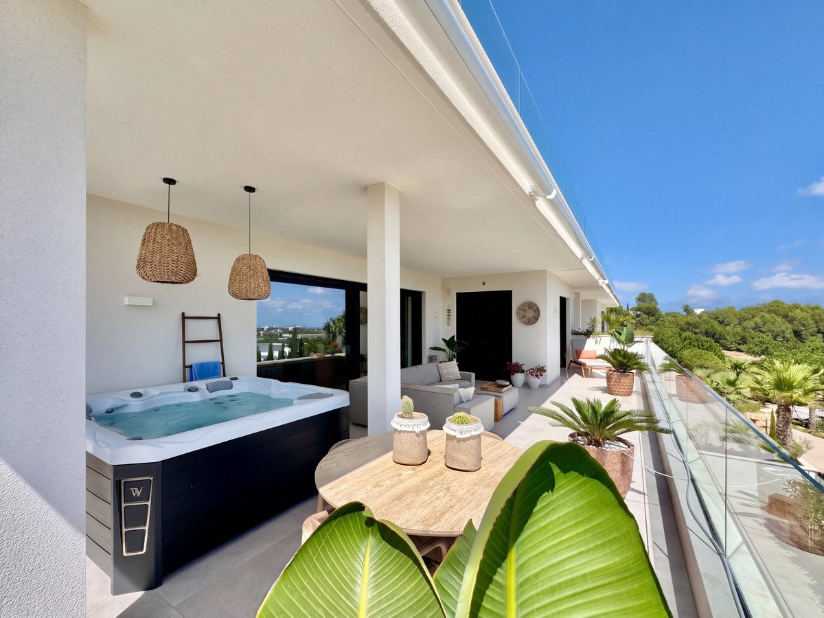 Modern balcony with a hot tub, comfortable seating, dining table, and scenic views of the sea and greenery.