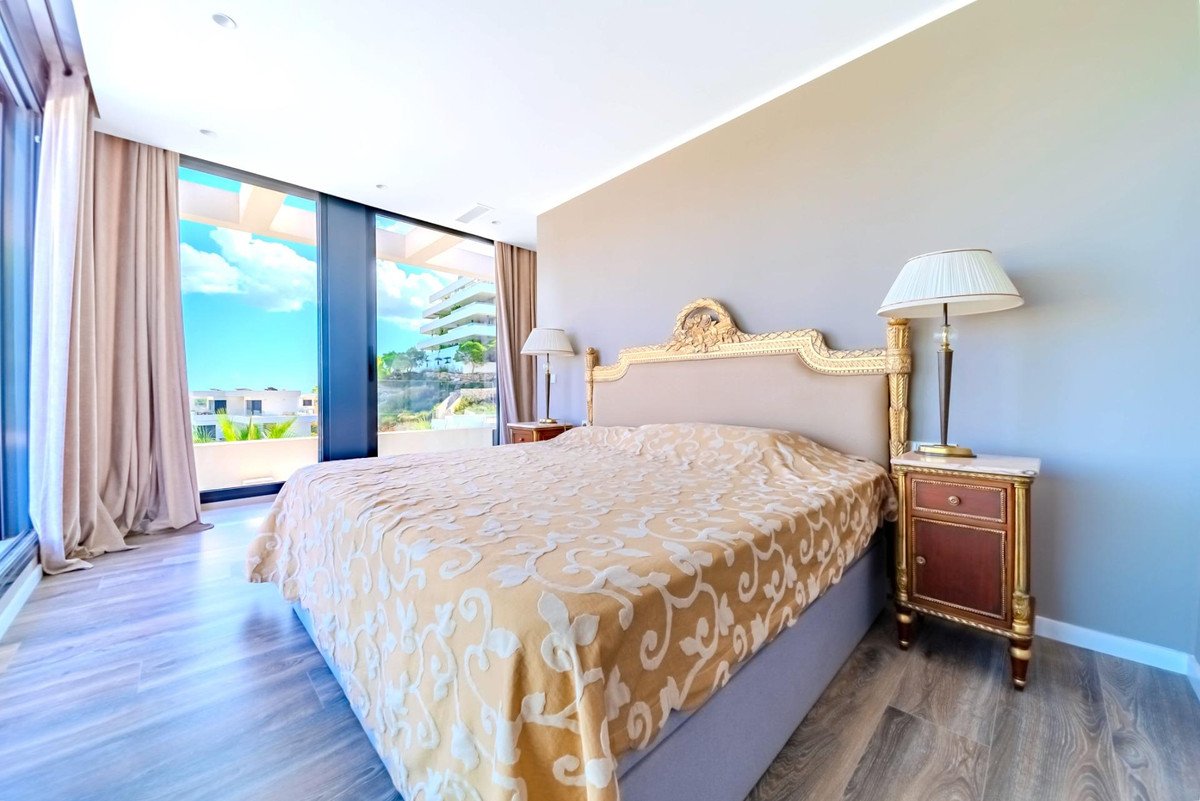 Luxurious bedroom with a large bed, ornate headboard, and large windows offering a beautiful sea and sky view.