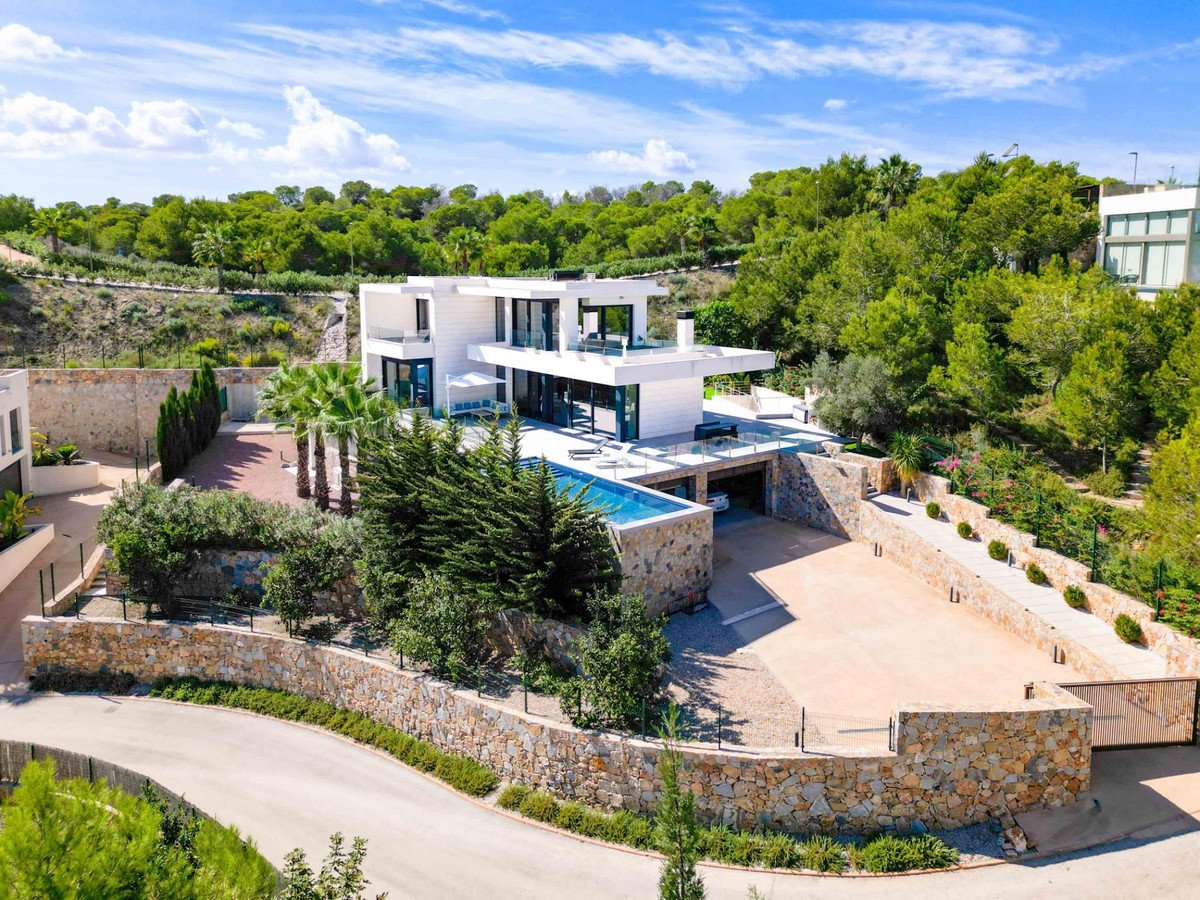 Modern white villa with a swimming pool, large driveway, and lush green trees under a blue sky.