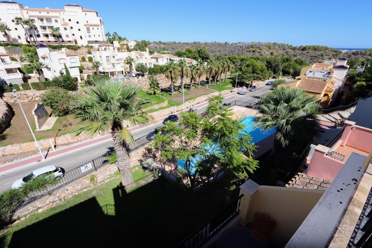 View from a balcony overlooking a swimming pool, palm trees, and residential buildings under a clear blue sky.
