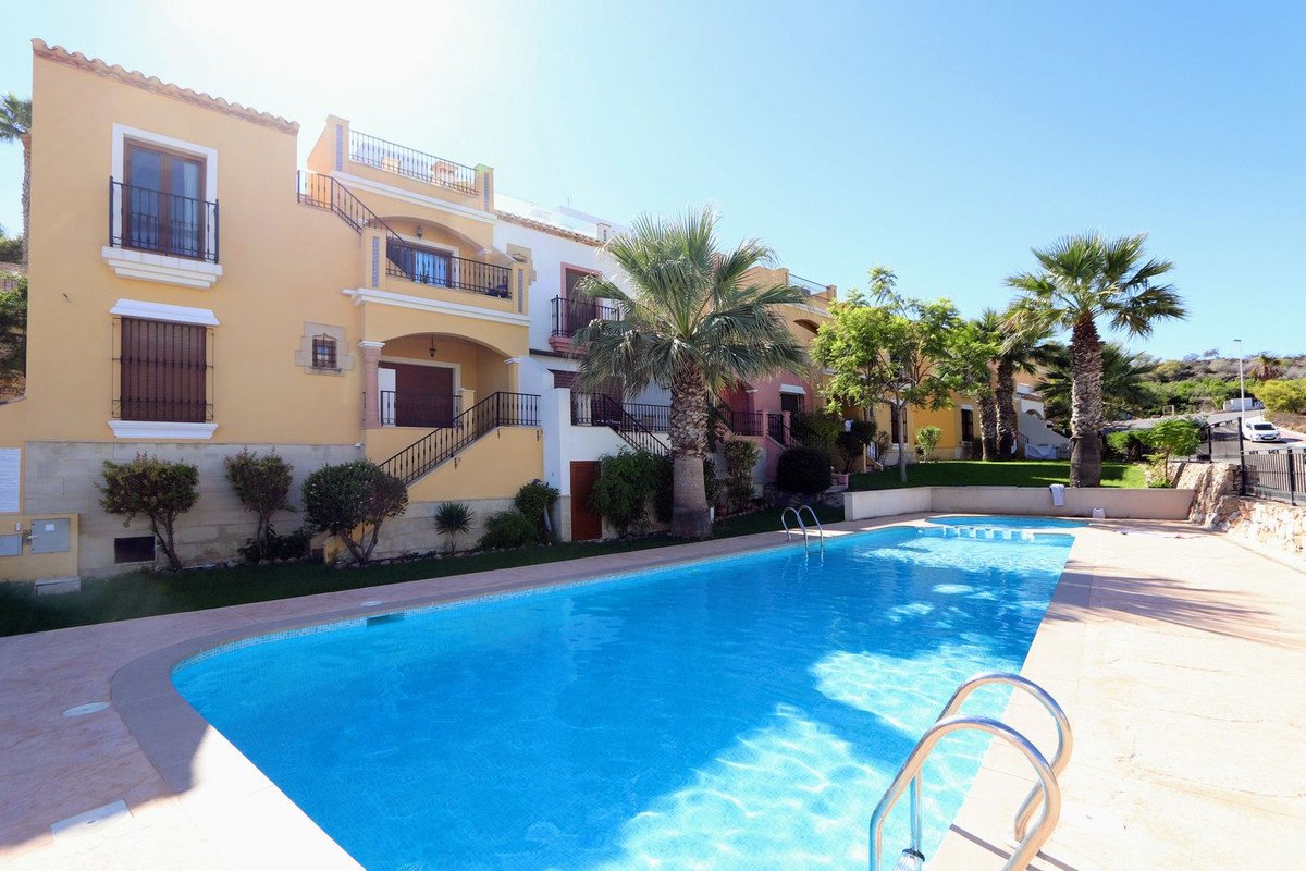 Bright blue swimming pool with ladders and surrounding buildings with balconies and palm trees on a sunny day.