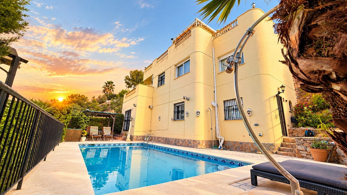 Exterior of a yellow villa with a swimming pool, lounge chairs, and a beautiful sunset view.