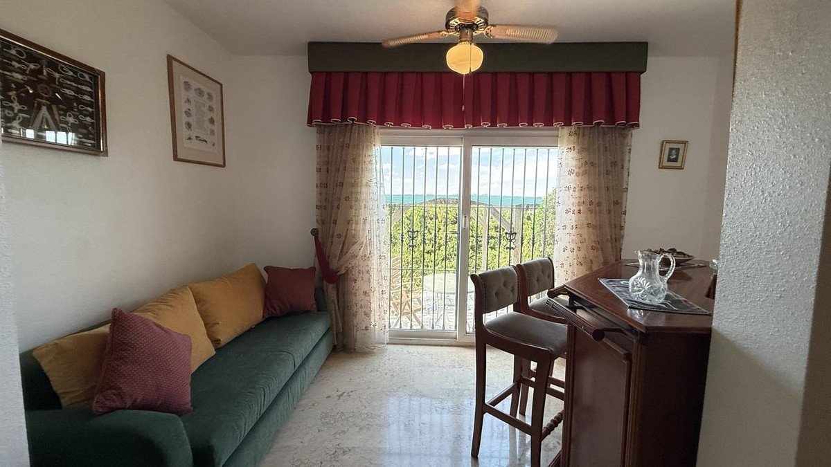 Living room with a green sofa, bar area, and sliding doors offering a scenic view of the sea and greenery.