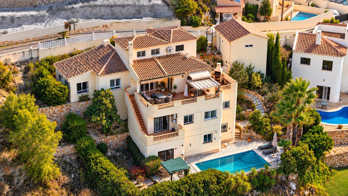 Aerial view of a multi-story villa with a swimming pool, lounge terrace, and outdoor grill, surrounded by lush greenery.