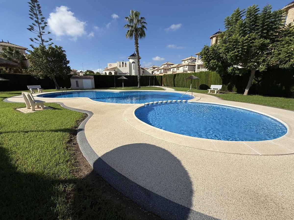 A beautiful communal swimming pool with blue water, surrounded by green grass and sun loungers, on a bright sunny day.