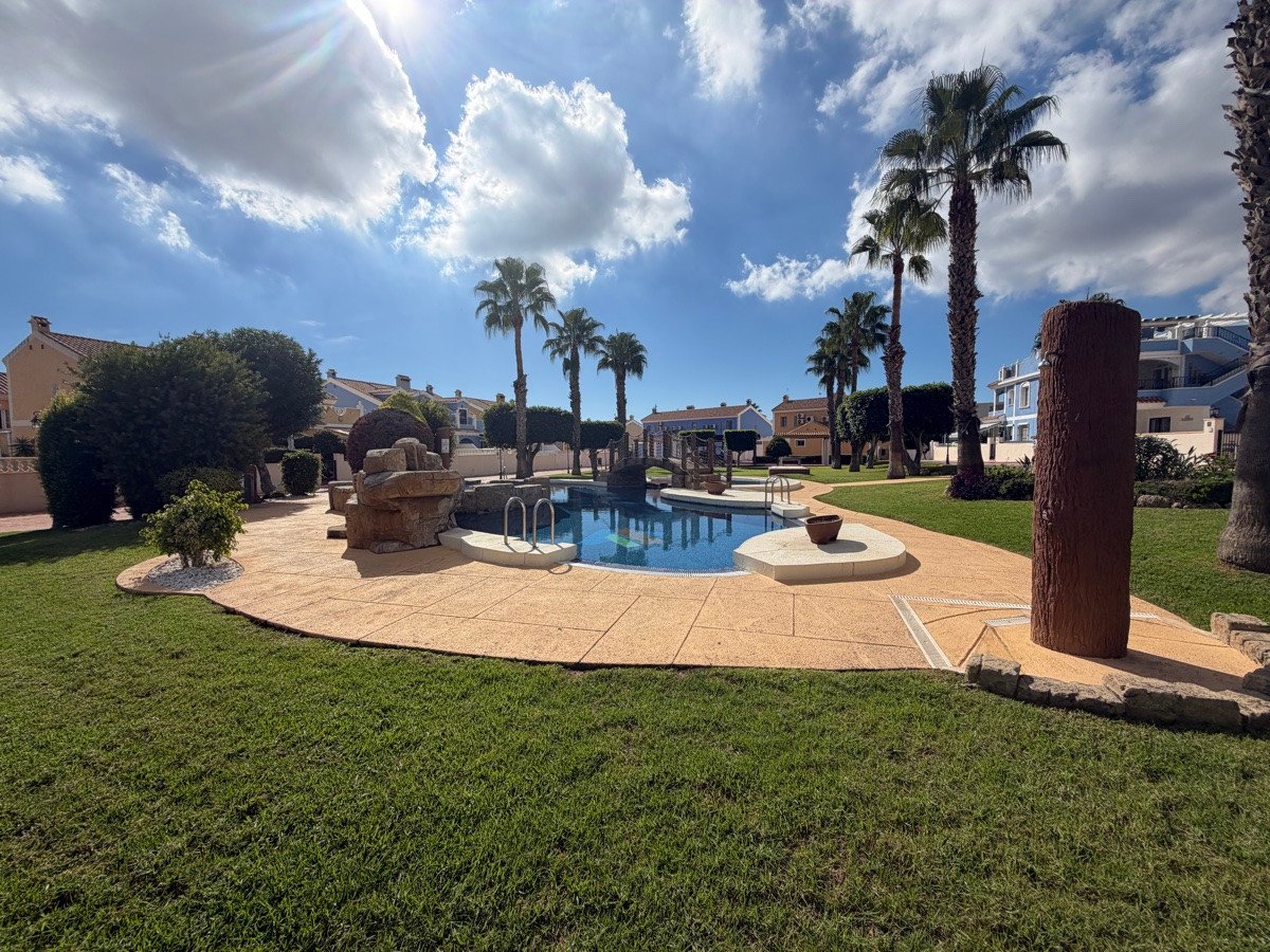 A sunny day shows a swimming pool with palm trees and a landscaped garden area.