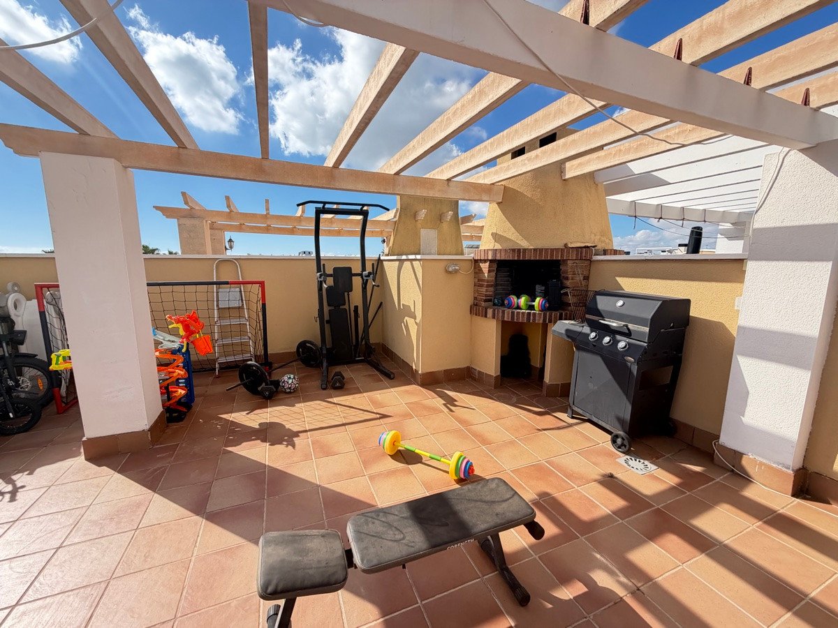Outdoor terrace with a grill, barbecue, weight bench, dumbbells, and a pull-up bar under a pergola.