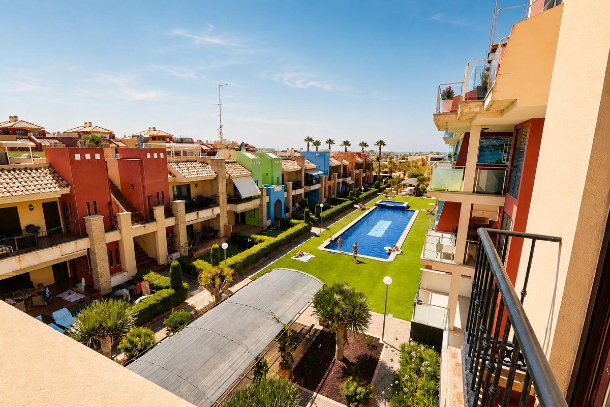 Colorful townhouse complex with a swimming pool and people sunbathing on a bright sunny day.