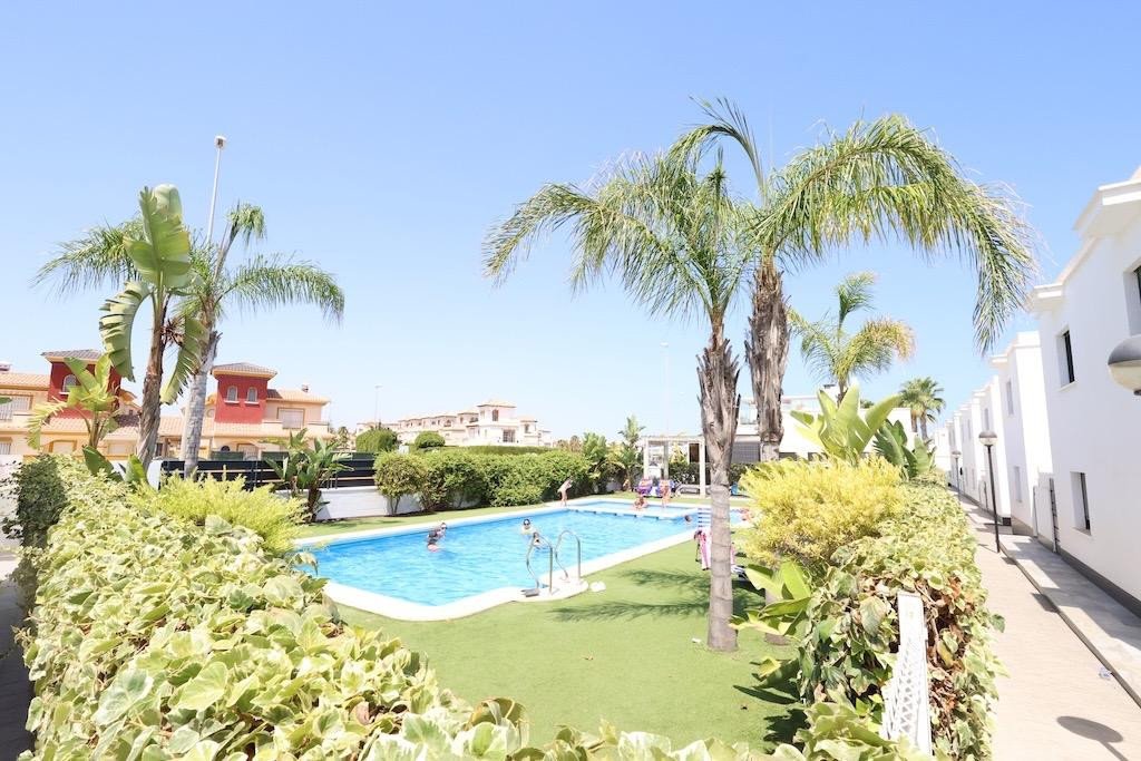 Luxurious swimming pool surrounded by tropical trees and white buildings under a clear blue sky