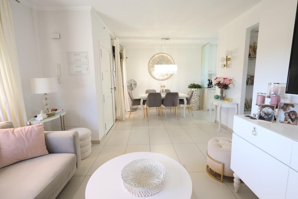Modern living room with dining area, featuring a white sofa, pink cushions, and a round coffee table with a decorative centerpiece