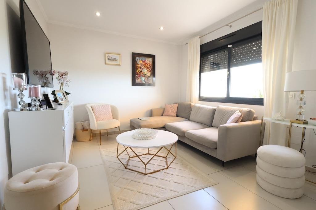 Modern living room featuring beige sofa, armchairs, and a geometric coffee table with large windows and light curtains