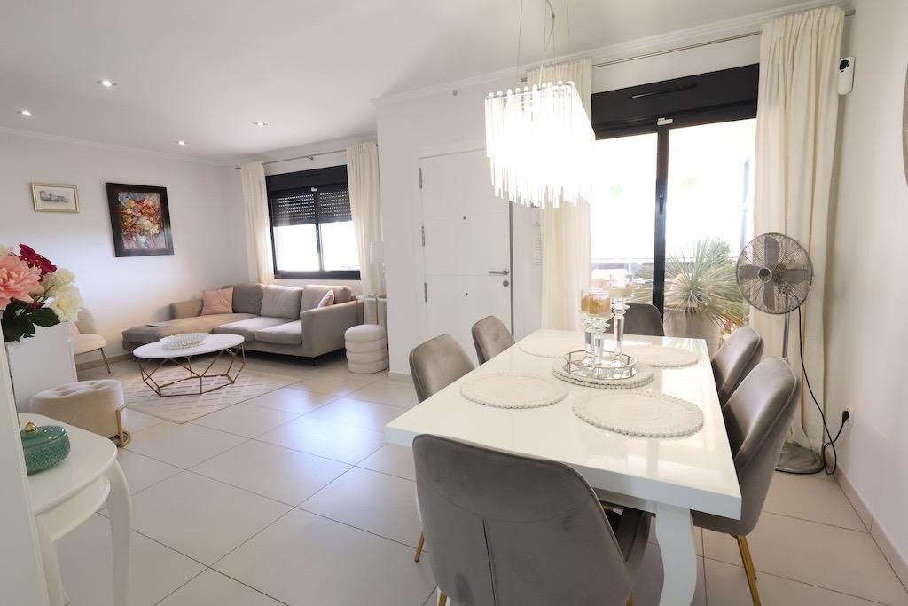Modern living and dining area with white furniture, chandelier, and large windows overlooking a balcony.