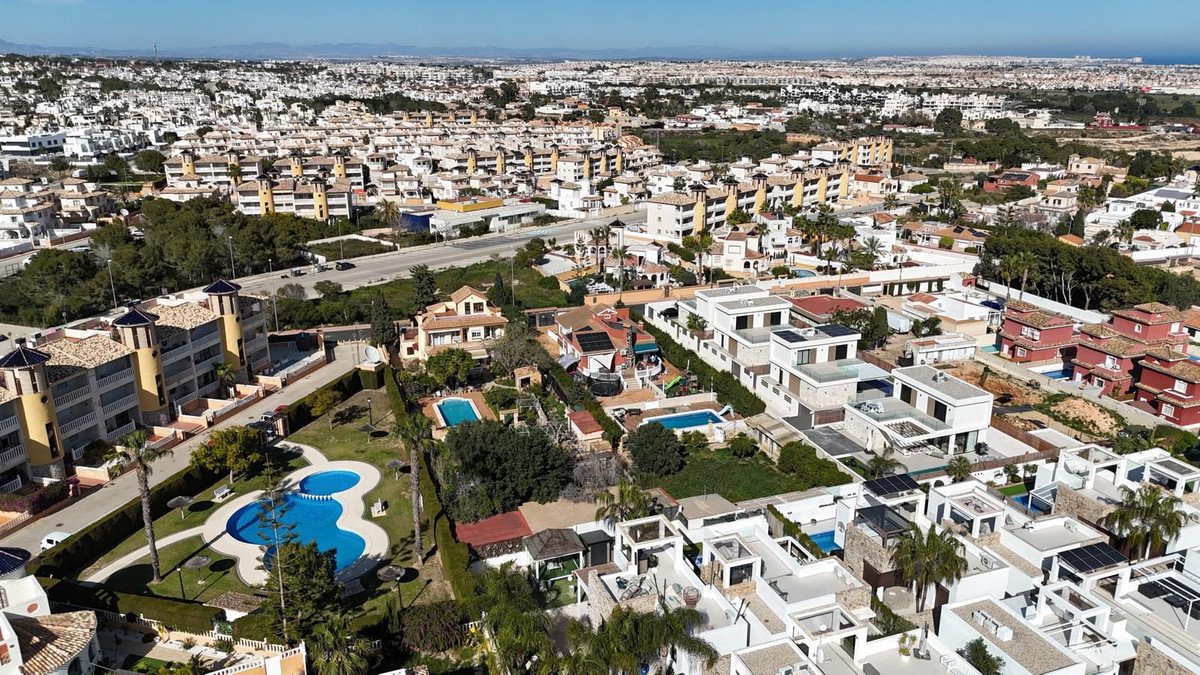 Aerial view of modern villas with pools in a dense urban development under a clear blue sky.