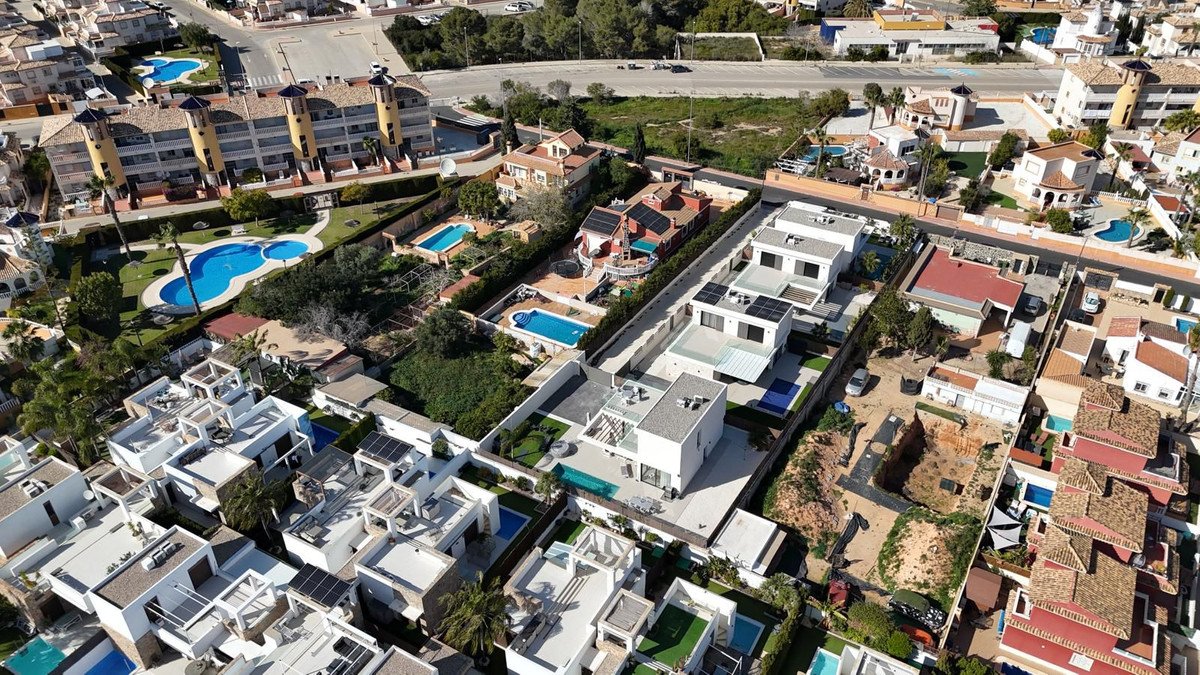 Aerial view of multiple modern villas and apartment buildings, many featuring private pools and solar panels, in a residential area.