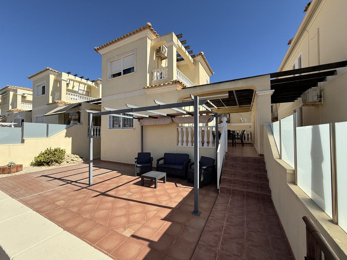Terrace with seating area under a pergola, steps leading up to a house entrance, and modern glass balustrades.