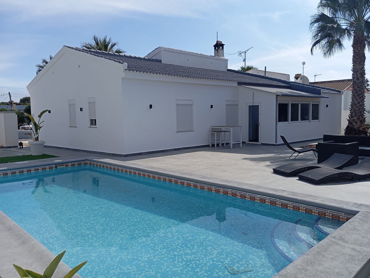 Modern white villa with private pool, patio, lounge chairs, and palm trees under blue sky.