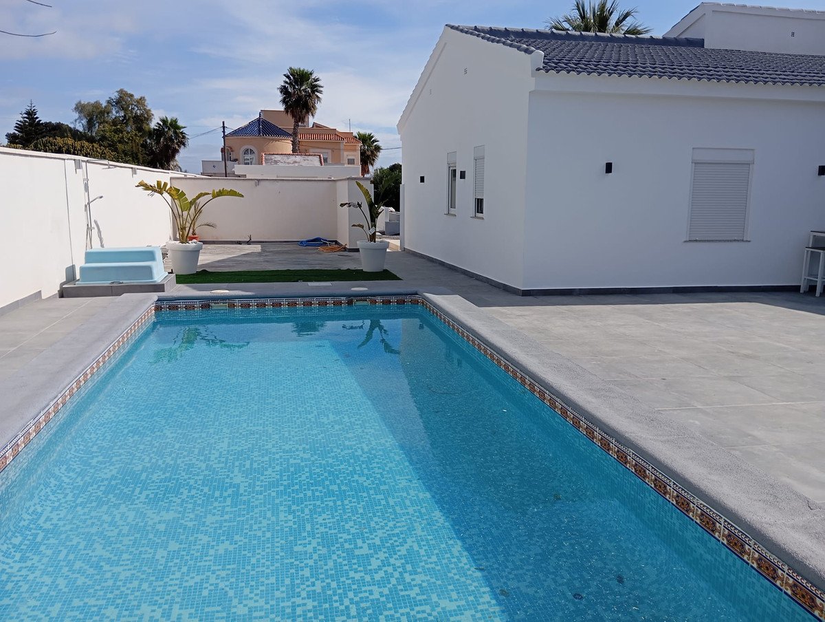 Modern white villa with private pool, tiled patio, and palm trees under blue sky.