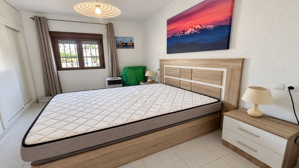 A bedroom with a large bed, mountain artwork on the wall, and a window with a view of trees.