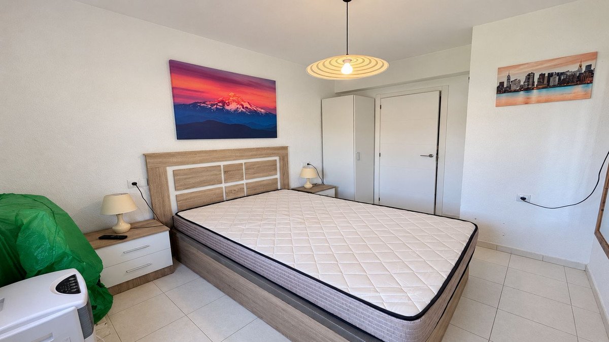 A bedroom with a large bed, bedside tables, a wardrobe, and wall art of mountains and a city skyline.