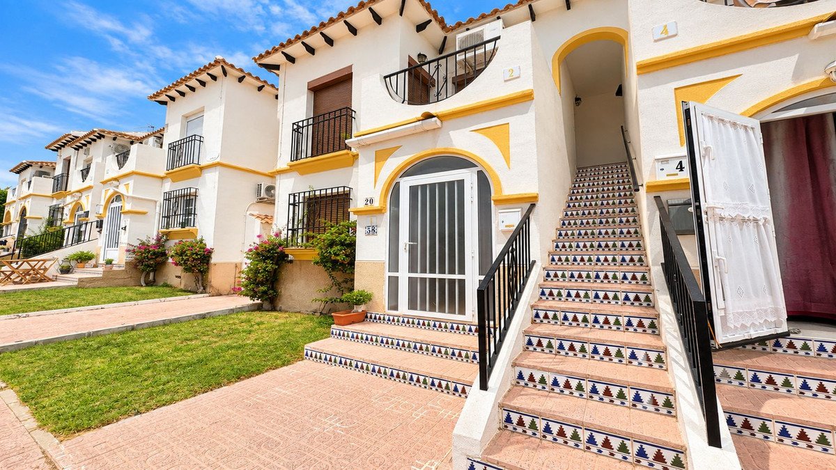 Terraced houses with decorative front steps, balconies, and green lawns under a blue sky.