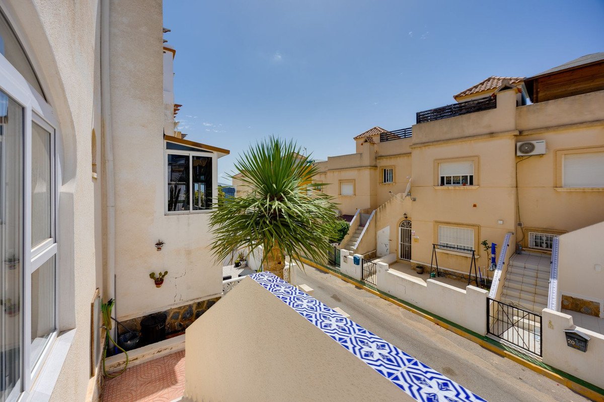 View from a balcony overlooking a street with palm trees and houses on a sunny day.