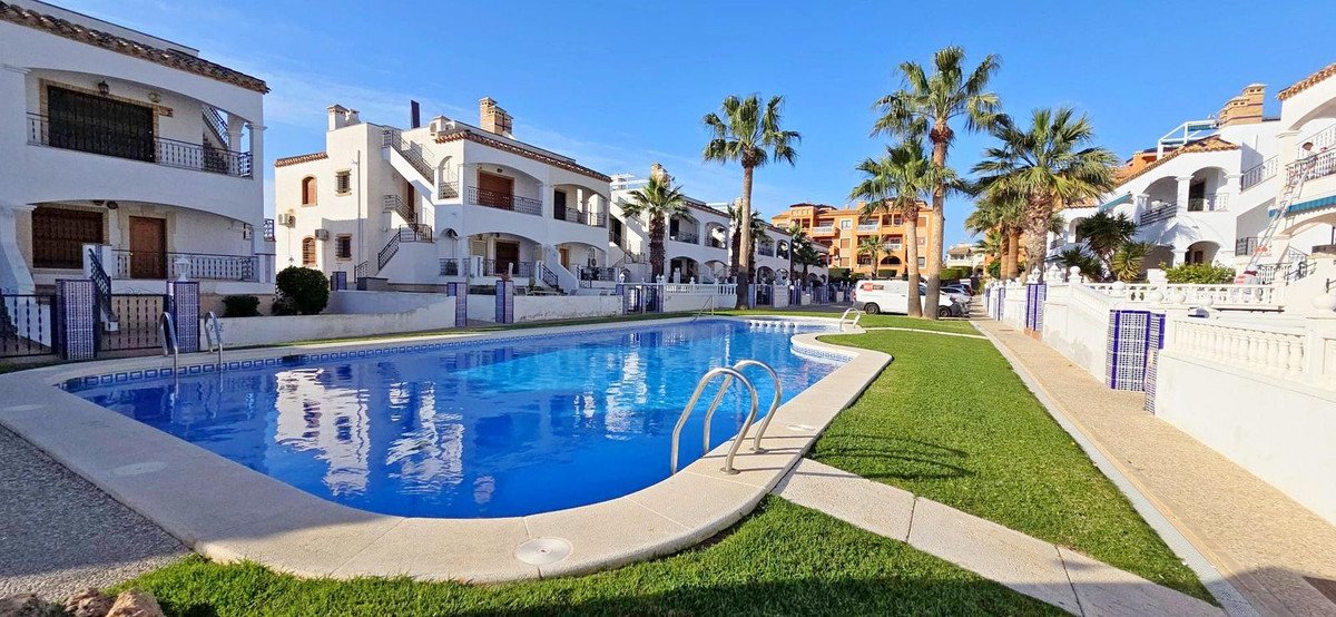 A sparkling blue swimming pool with palm trees and white apartment buildings under a clear blue sky.