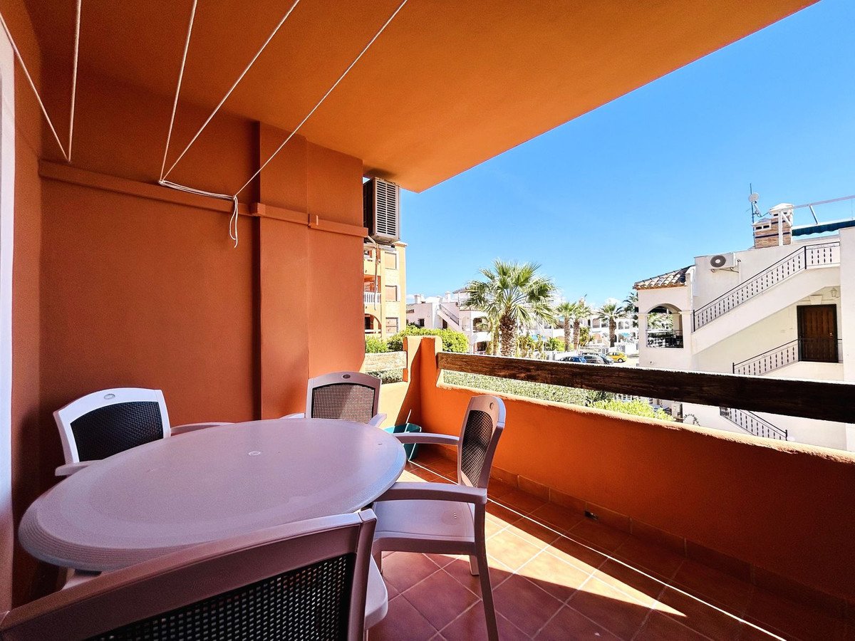 A sunny terrace with a table and chairs, overlooking palm trees and buildings under a clear blue sky.