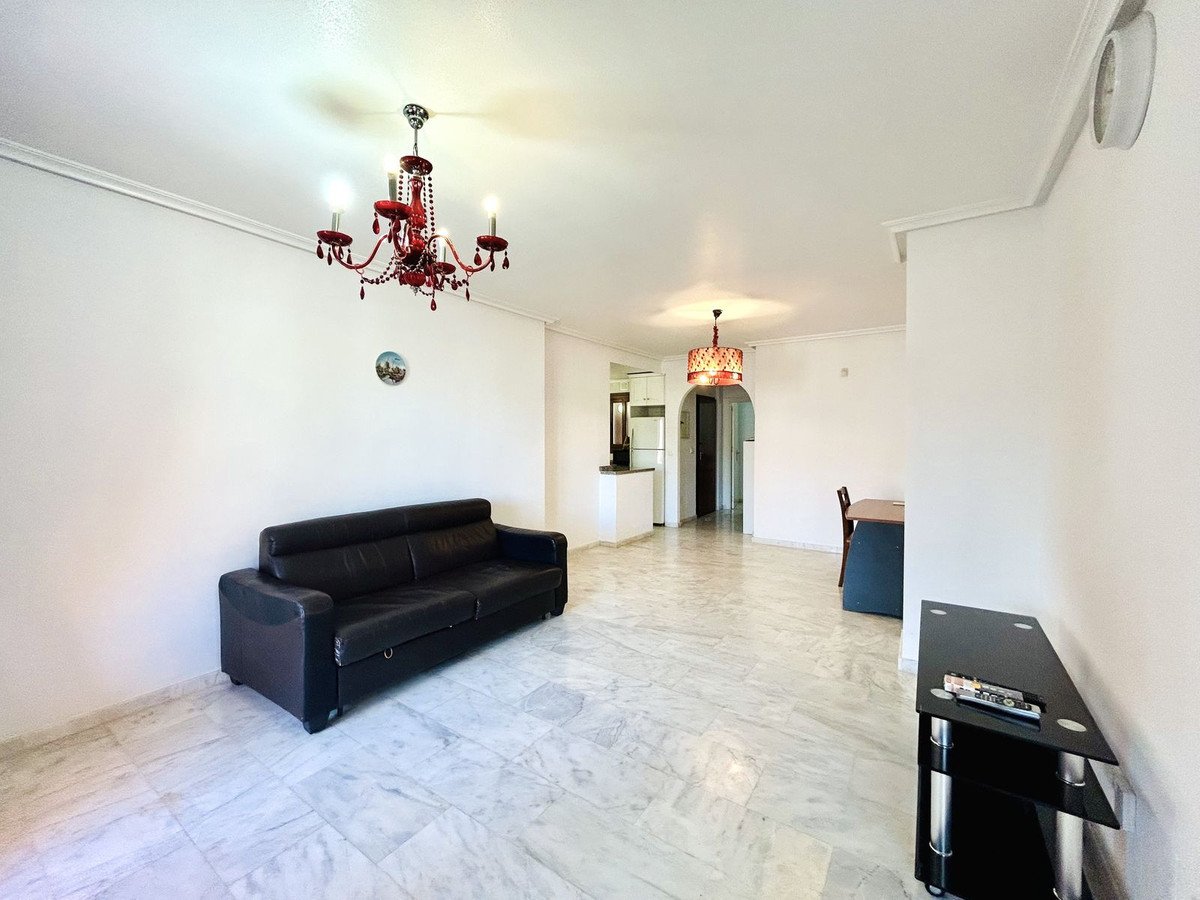 Spacious living area with a black leather sofa, marble floors, and a dining table visible in the background.
