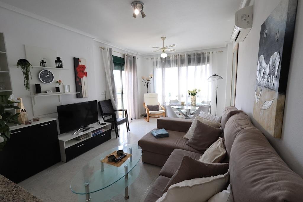 Modern living and dining area with comfortable sofa, TV, dining table, and large windows.