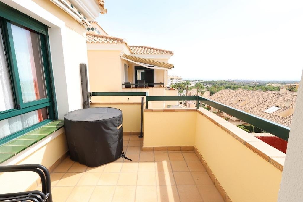 View from a spacious balcony with tiled flooring, overlooking rooftops and greenery. Includes outdoor furniture cover.