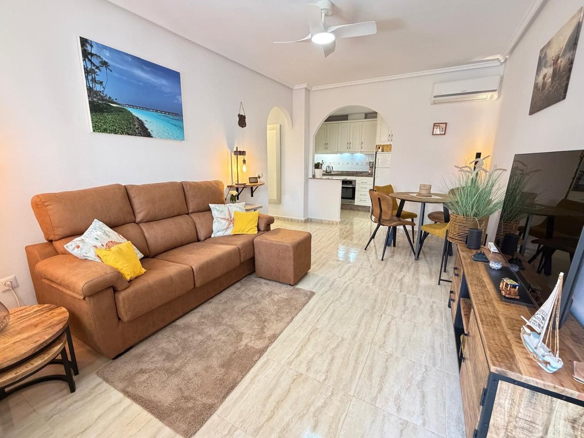 Modern living and dining room with a comfortable sofa, dining table, and kitchen visible in the background.